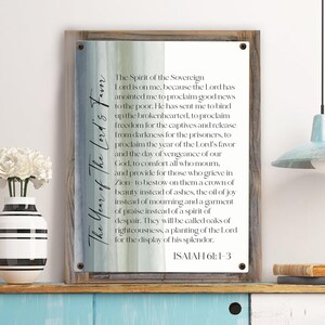 May include: A wood framed print with a watercolor background and white text. The text reads "The Year of the Lord's Favor" and includes a bible verse from Isaiah 61:1-3.