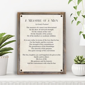 May include: A framed print with the text "A Measure of a Man" by Grady Poulard. The poem is printed on a cream-colored background and framed in a rustic wooden frame. The print is displayed on a white shelf.
