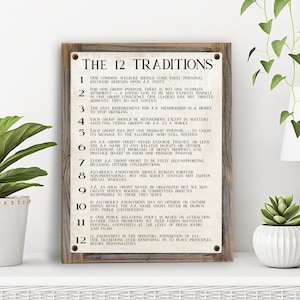 May include: A rustic wooden sign with the text "The 12 Traditions" and a list of 12 traditions for Alcoholics Anonymous. The sign is painted in a cream color with brown text and a brown wooden frame.