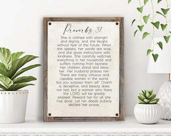 May include: A wood sign with a white background and black text. The sign features a quote from Proverbs 31 about a virtuous woman. The text reads "Proverbs 31 She is clothed with strength and dignity, and she laughs without fear of the future When she speaks, her words are wise, and she gives instructions with kindness. She carefully watches everything in her household and suffers nothing from laziness. Her children stand and bless her Her husband praises her There are many virtuous and capable women in the world, but you surpass them all! Charm is deceptive, and beauty does not last, but a woman who fears the LORD will be greatly praised Reward her for all she has done Let her deeds publicly declare her praise"