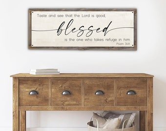 May include: A rustic wooden sign with a white background and black text. The sign reads "Taste and see that the Lord is good, blessed is the one who takes refuge in him. Psalm 34:8".