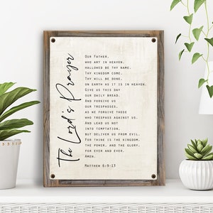 May include: A rustic wooden sign with a white background and black text. The sign features the Lord's Prayer, with the text "The Lord's Prayer" written vertically on the left side of the sign. The text includes the words "Our Father, who art in heaven, hallowed be thy name." and "Matthew 6:9-13".