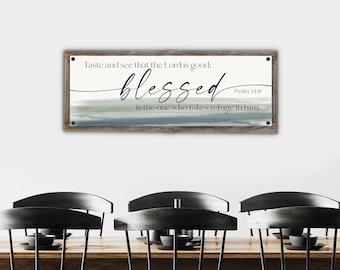 May include: A rectangular wooden sign with the words "Taste and see that the Lord is good: blessed is the one who takes refuge in him." in black script. The background has watercolor-style blue and green stripes.