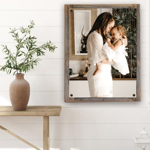 May include: A framed photograph of a mother and daughter in white dresses, embracing and smiling. The photo is set against a rustic wooden background.