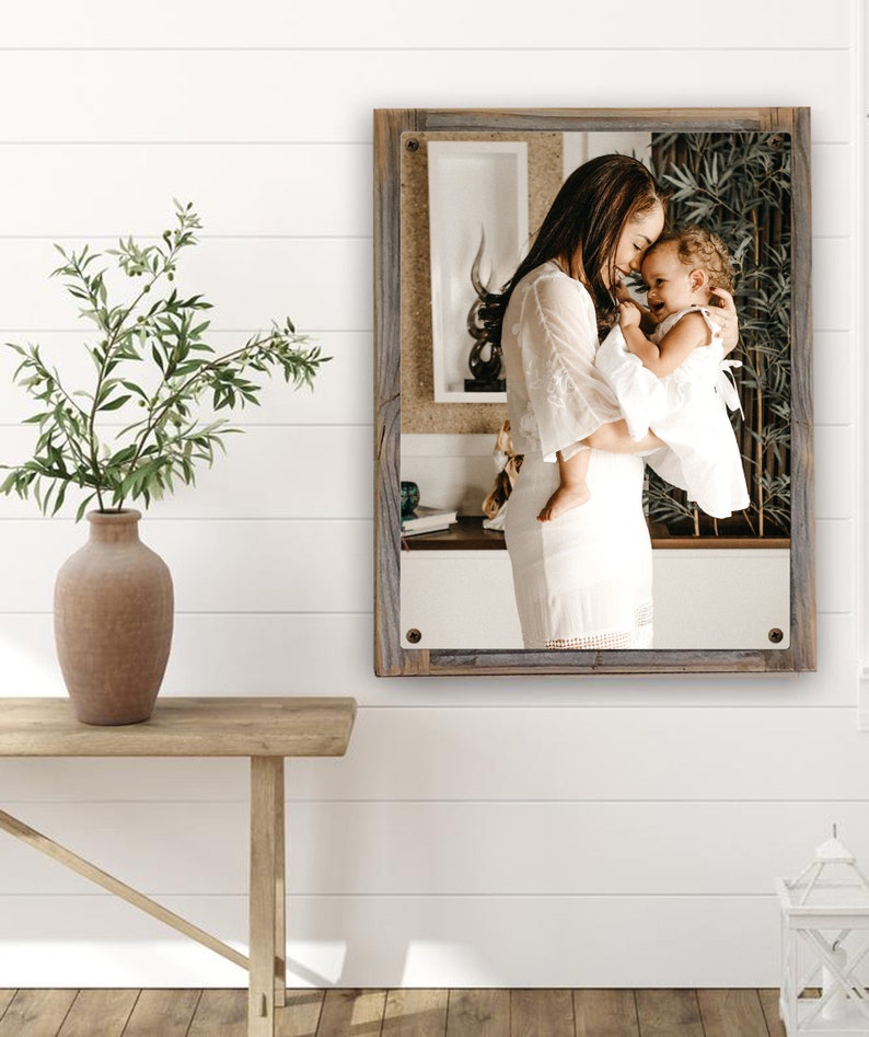 May include: A framed photograph of a mother and daughter in white dresses, embracing and smiling. The photo is set against a rustic wooden background.