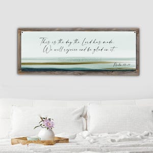 May include: A framed wall art piece with a watercolor landscape design in shades of blue, green, and brown. The artwork features the text "This is the day the Lord has made. We will rejoice and be glad in it." and "Psalm 118-24."