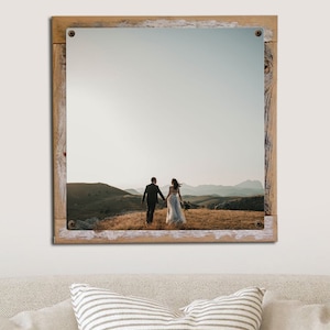 May include: A framed photograph of a couple walking away from the camera on a grassy hilltop. The couple is wearing wedding attire and the background is a mountain range with a cloudy sky.