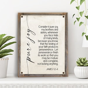 May include: A framed print with a white background and black text. The text reads "Consider it pure joy, my brothers and sisters, whenever you face trials of many kinds, because you know that the testing of your faith produces perseverance. Let perseverance finish its work so that you may be mature and complete, not lacking anything. JAMES 1:2-4".