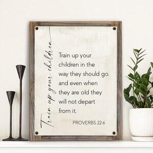 May include: A white canvas sign with a wood frame and the text "Train up your children in the way they should go. And even when they are old they will not depart from it. Proverbs 22:6"
