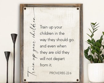 May include: A white canvas sign with a wood frame and the text "Train up your children in the way they should go. And even when they are old they will not depart from it. Proverbs 22:6"