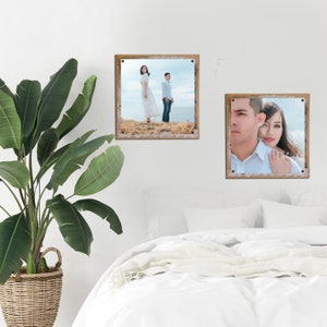 May include: Two framed photographs of a couple. The first photo shows the couple standing on a grassy hill, looking out at the ocean. The second photo shows the couple looking at the camera, with the woman resting her head on the man's shoulder.