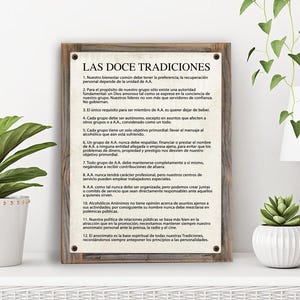 May include: A framed print with a rustic wood frame and a white background. The print features the text "LAS DOCE TRADICIONES" in a black font. The text is in Spanish and lists the 12 traditions of Alcoholics Anonymous.