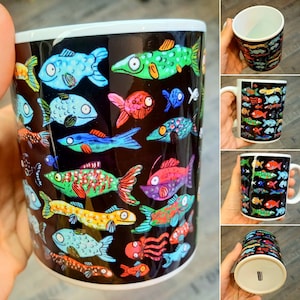 Könnte beinhalten: Eine schwarze Keramiktasse mit einem farbenfrohen Fischdesign. Die Fische sind in verschiedenen Blautönen, Grün-, Rot- und Gelbtönen bemalt. Die Tasse ist ein tolles Geschenk für Fischliebhaber.