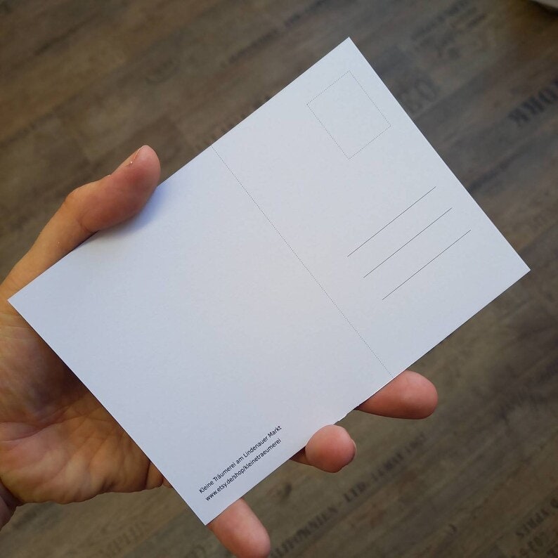 May include: A white postcard with a blank front and a back with a space for a stamp, an address, and a message. The back also includes the text "Kleine Tr&auml;ume am Lindauer Markt" and a website address.
