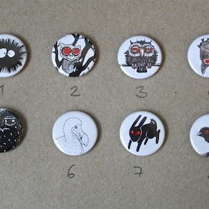 Può includere: Otto bottoni rotondi in bianco e nero con diverse illustrazioni di animali. I bottoni sono numerati da 1 a 8. Gli animali includono una creatura pelosa, un gufo, un pipistrello, un dinosauro, un dodo, un coniglio, un uccello e una creatura con occhi grandi.