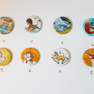 Può includere: Otto bottoni rotondi con diverse illustrazioni. I bottoni sono bianchi con uno sfondo giallo, arancione o blu. Le illustrazioni includono una sirena, un leone, un drago, una volpe, un unicorno, un asino e una volpe.