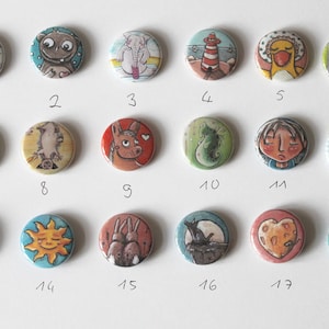 Può includere: Set di 18 bottoni rotondi colorati con varie illustrazioni di animali e natura. Ogni bottone presenta un design diverso, tra cui un gatto, un sole, una volpe, un cavalluccio marino, un cuore e altro ancora.