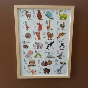 Könnte beinhalten: Ein farbenfroher Alphabet-Chart mit Illustrationen von Tieren für jeden Buchstaben. Der Chart ist in einem hellen Holzrahmen gerahmt.