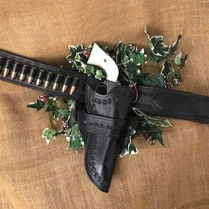 May include: A black leather gun belt with a holster and a silver and ivory revolver. The belt has a row of bullets attached to it.
