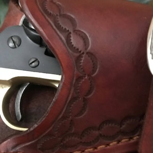 May include: A brown leather holster with a decorative pattern. A black and silver revolver is partially visible inside the holster.