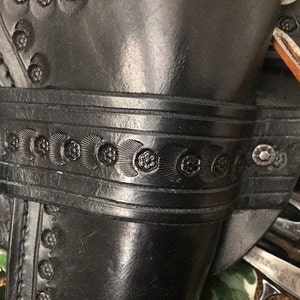 May include: A black leather holster with intricate floral designs and metal rivets. The holster is designed to hold a revolver.