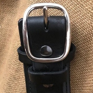 May include: A black leather belt with a silver buckle. The buckle has a smooth, rounded edge and a small, round button in the center.
