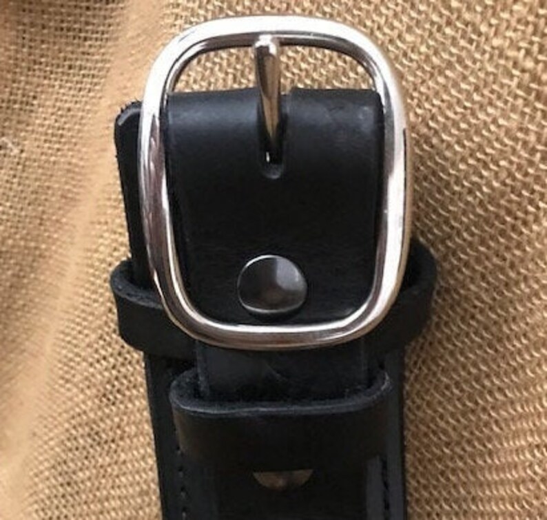 May include: A black leather belt with a silver buckle. The buckle has a smooth, rounded edge and a small, round button in the center.