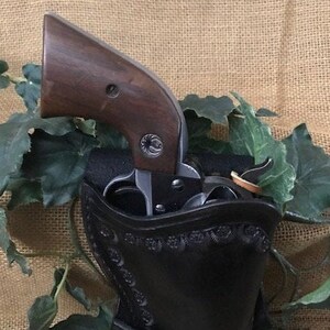 May include: A black leather holster with intricate stitching and a brown wooden-handled revolver inside.