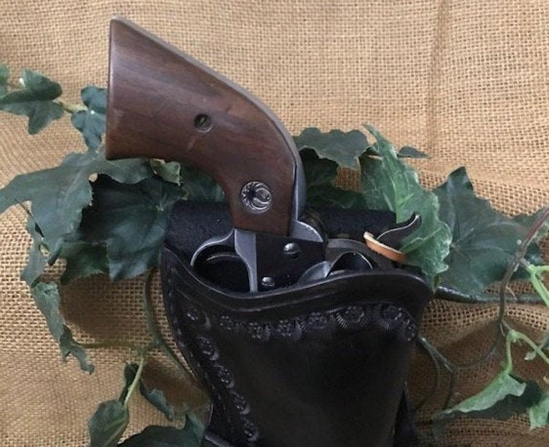 May include: A black leather holster with intricate stitching and a brown wooden-handled revolver inside.