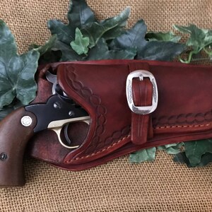May include: A brown leather holster with a silver buckle and a small black and silver revolver inside.