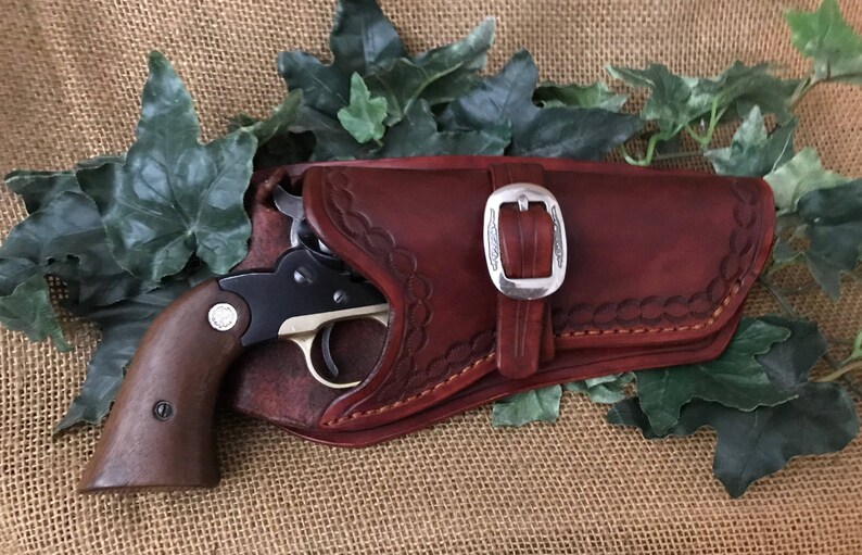 May include: A brown leather holster with a silver buckle and a small black and silver revolver inside.