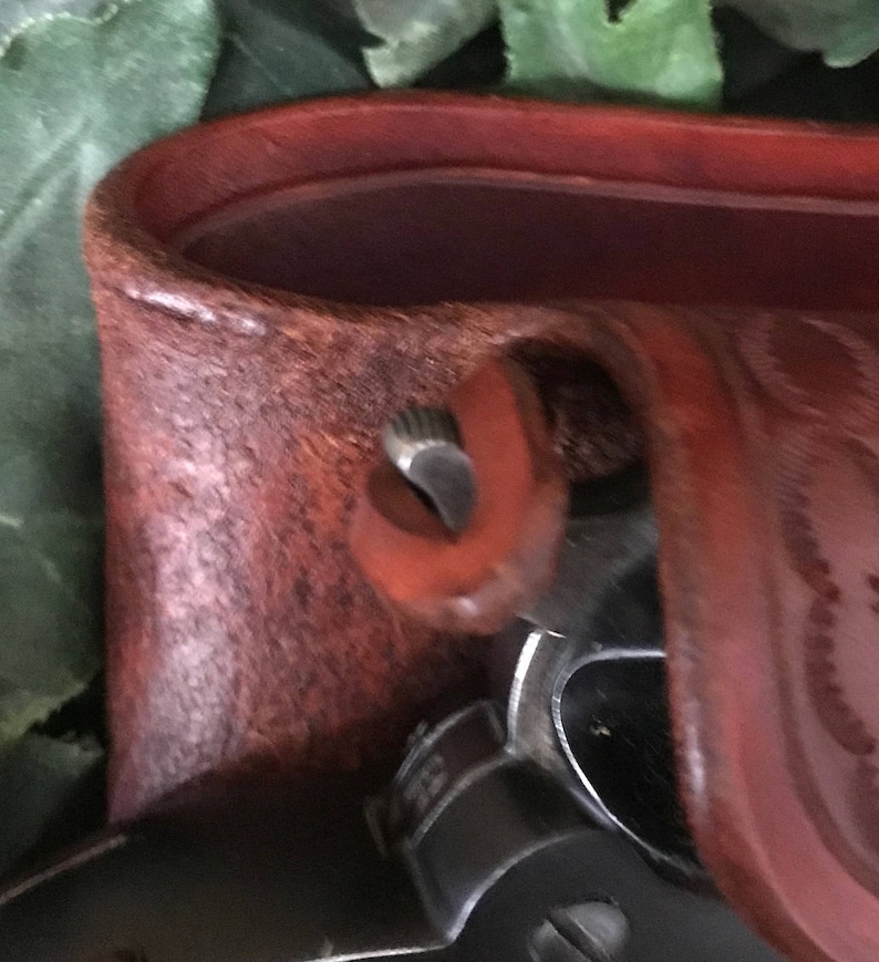 May include: Close-up of a brown leather holster with a metal snap closure. The holster is designed to hold a firearm.