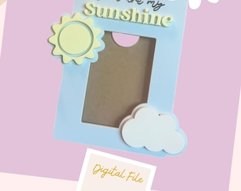 以下が含まれることがあります： 黄色の太陽と白い雲、そして「You are my Sunshine」という文字が書かれた薄い青色の写真フレーム。フレームはデジタルファイルです。