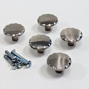 May include: Five silver-toned cabinet knobs with a scalloped edge and a round base. The knobs are arranged in a semi-circle with screws in the center of the image.
