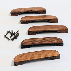 May include: Five wooden cabinet pulls with a curved design, in a rich brown color. The pulls are accompanied by a set of small screws, suggesting they are ready for installation. The pulls are made of solid wood.