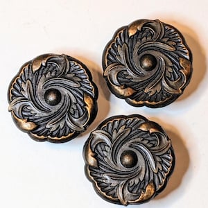May include: Three circular buttons featuring a dark metallic finish with raised bronze-toned highlights. Each button displays a detailed, swirling acanthus leaf pattern radiating from a central circular point, creating a textured, dimensional appearance.