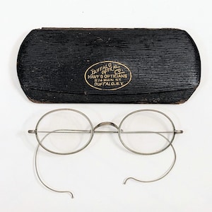 May include: Antique round eyeglasses with wire frames and a black case. The case has a gold emblem with the text "Buffalo Optical Co. Hant & Opticians 514 Main St. Buffalo, N.Y."