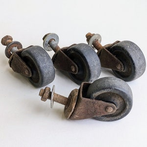 May include: Four rusty metal caster wheels with black rubber tires. The wheels are attached to metal stems with a nut and washer.