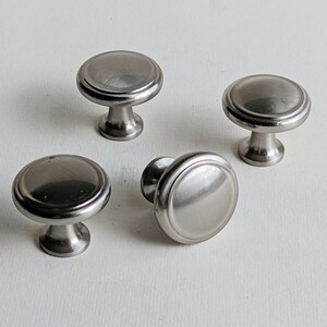 May include: Four silver cabinet knobs with a round, slightly raised, center and a smooth, slightly rounded, base.