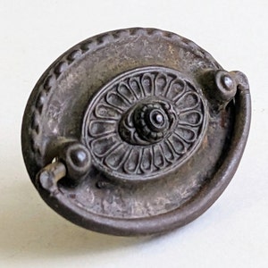 May include: An antique oval-shaped cabinet pull with a decorative floral design. The pull is made of metal and has a dark brown finish.