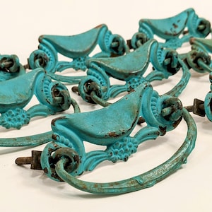 May include: A collection of turquoise-colored, ornate drawer pulls with a distressed finish. Each pull features a curved handle, decorative floral elements, and mounting hardware. The hardware is made of metal.