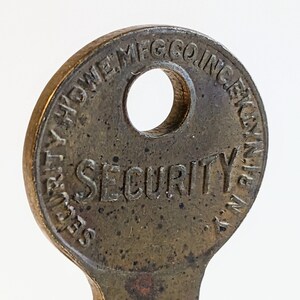 May include: A brass key with a round head and a keyhole. The head of the key is engraved with the text "SECURITY" and "NEW HAVEN MFG CO INC".