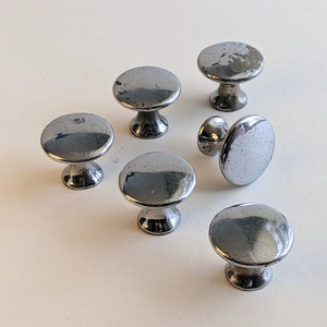 May include: Six silver metal cabinet knobs with a smooth, rounded surface. The knobs have a classic design and are perfect for adding a touch of elegance to any room.