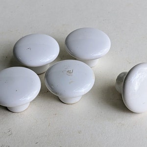 May include: Five white ceramic cabinet knobs with a rounded top and a short stem.