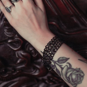 May include: A black chain bracelet with multiple links and a rose tattoo on the wearer's arm.