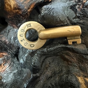May include: A vintage brass key with a circular head and a rectangular bit. The head is stamped with the numbers "2169" and the letter "H". The key has a worn, antique appearance.