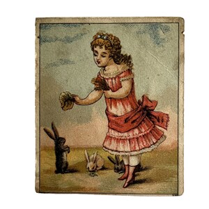 May include: A young girl in a pink dress with a white lace collar and a red ribbon around her waist is feeding three rabbits. The rabbits are white and brown. The girl is holding a bunch of green leaves in her hand. The background is a light blue sky with white clouds.