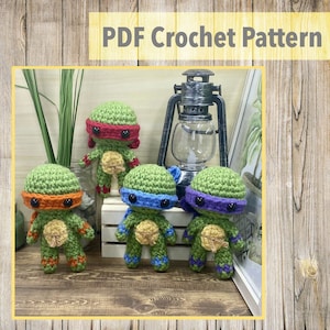 Pode incluir: Quatro figuras de amigurumi das Tartarugas Ninja Adolescentes crochetadas. Cada figura usa uma máscara de uma cor diferente: vermelho, azul, roxo e laranja. As figuras estão sentadas em uma superfície de madeira na frente de uma lanterna.