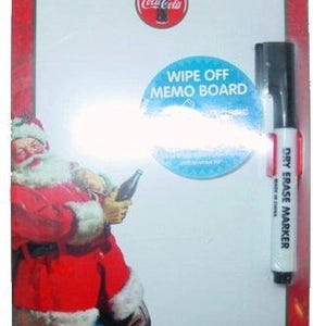 Op de afbeelding: Een rechthoekig Coca-Cola memobord met een rode rand, met een Santa Claus afbeelding en een Coca-Cola logo. Inclusief een whiteboard marker. Het bord heeft de tekst "WIPE OFF MEMO BOARD".