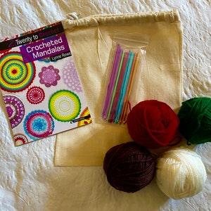 Pode incluir: Um kit de crochê com um livro intitulado "Twenty to Crochet Crocheted Mandalas" de Lynne Rowe, uma bolsa de agulhas de crochê coloridas e quatro novelos de lã em vermelho, verde, marrom e branco.